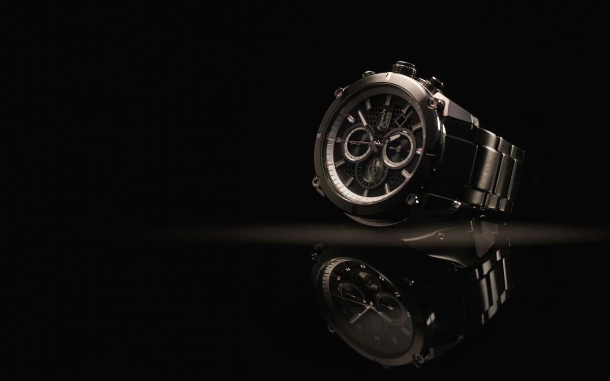 A silver chronograph watch on a black surface, its reflection below