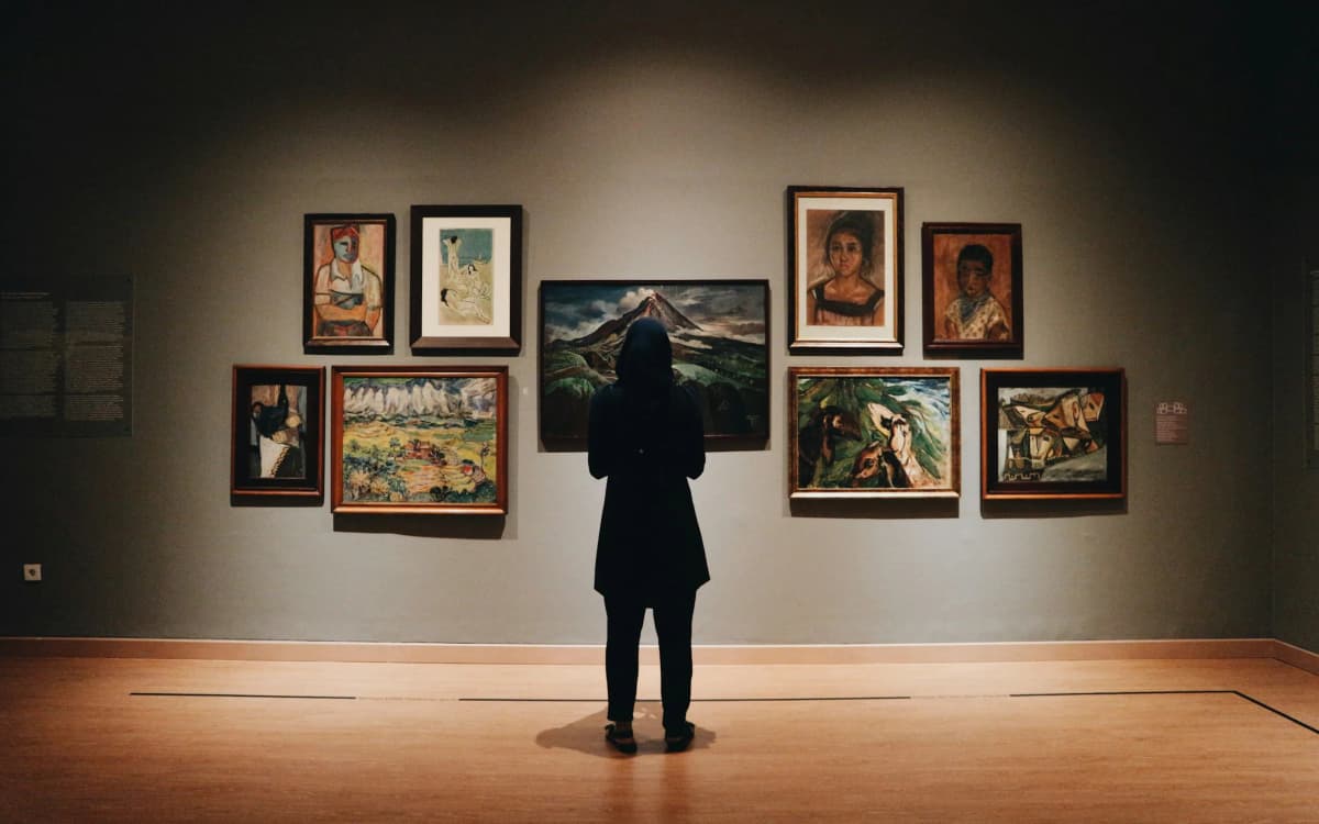 A visitor standing alone before a wall of framed paintings