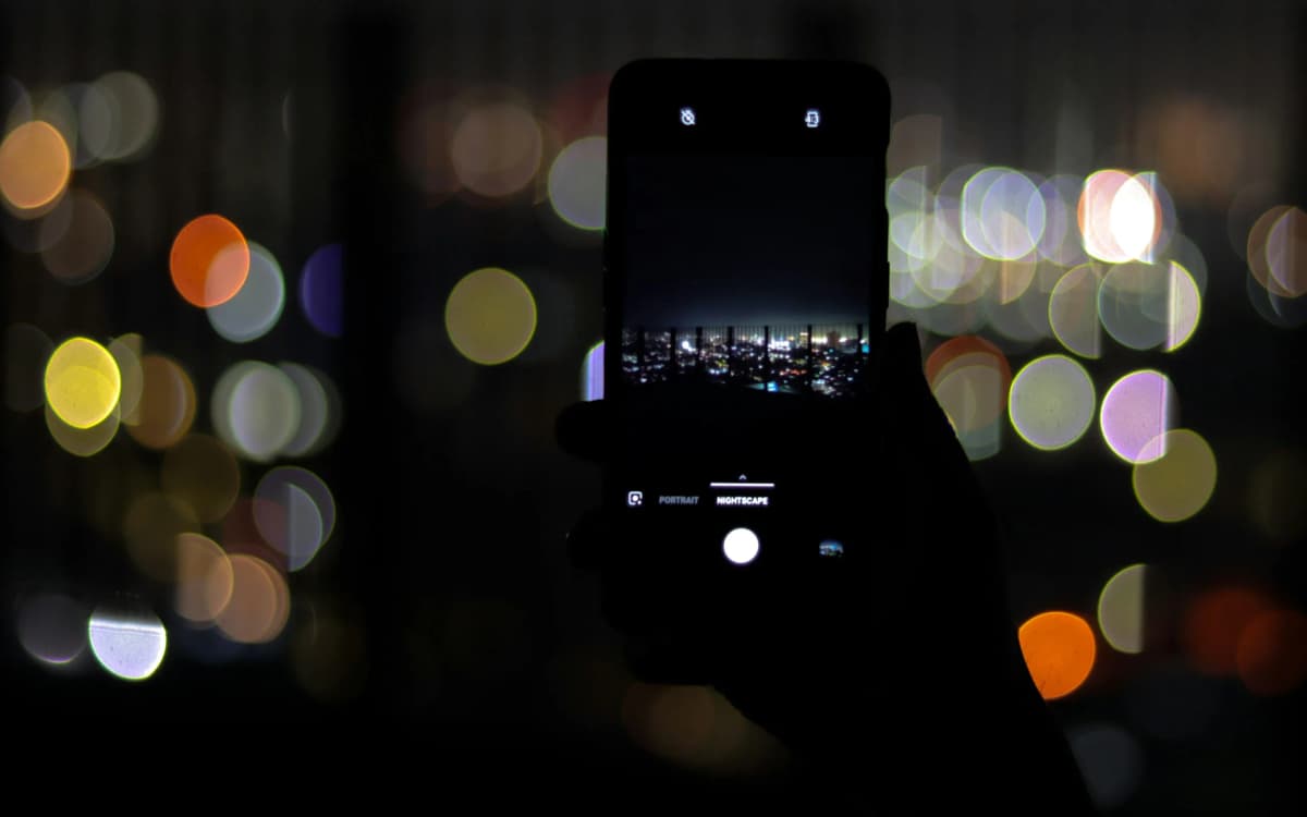 A hand holding a phone that films a city skyline at night